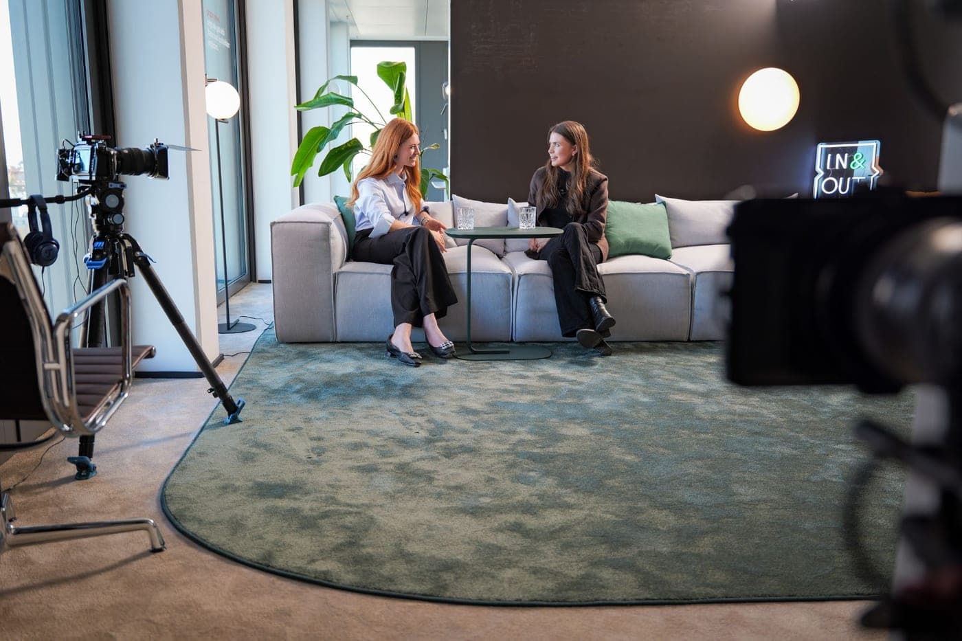 Videodreh im In&Out Studio — zwei Gesprächspartnerinnen auf dem Sofa, Kamera im Vordergrund